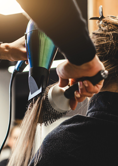 Frau mit langem Haar erhält Styling mit Föhn beim Friseurbesuch