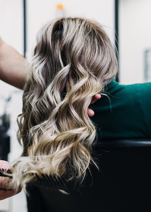 Frau mit welligen Haaren und Strähnchen beim Friseur